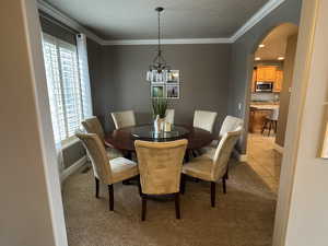 Dining room featuring light carpet, a chandelier, ornamental molding, and arched walkways