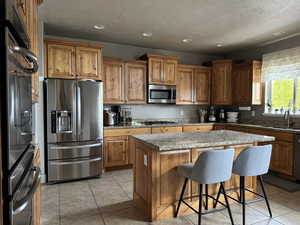 Kitchen featuring stainless steel appliances, a kitchen island, a kitchen bar, light tile patterned floors, and wood finish cabinets