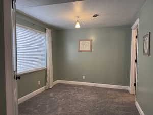Unfurnished room featuring a textured ceiling and dark colored carpet