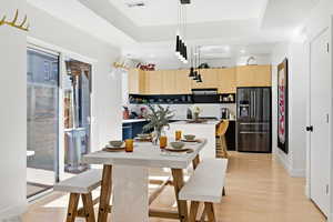 Kitchen featuring light wood finish cabinets, light countertops, refrigerator with ice dispenser, light wood finished floors, and pendant lighting