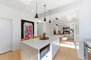 Kitchen featuring a kitchen island, black microwave, pendant lighting, light wood-type flooring, and a tray ceiling
