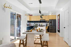 Kitchen with light wood finish cabinets, black fridge, light wood-type flooring, pendant lighting, and light countertops