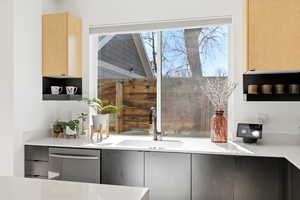 Kitchen with stainless steel dishwasher, light stone countertops, light wood finish cabinetry, and modern cabinets