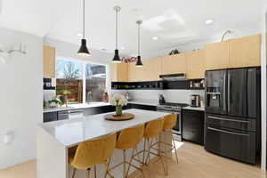 Kitchen with light wood finish cabinetry, stainless steel appliances, light stone counters, and decorative light fixtures
