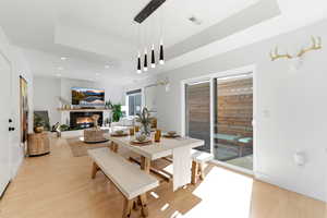 Dining space with a tray ceiling, a glass covered fireplace, recessed lighting, and light wood-style floors