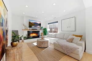 Living room with light wood-type flooring, a glass covered fireplace, and recessed lighting