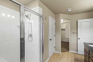 Full bathroom featuring a spacious closet, vanity, a shower stall, and light tile patterned floors