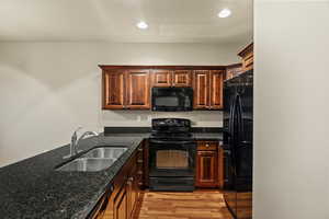 Kitchen with black appliances, dark stone counters, light wood-type flooring, and recessed lighting