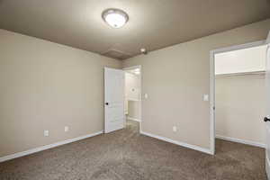 Unfurnished bedroom with dark colored carpet, a textured ceiling, and a walk in closet
