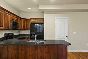 Kitchen with a peninsula, black appliances, dark stone counters, recessed lighting, and dark wood-style flooring. Half bath door