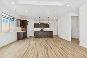 Kitchen featuring dark wood finish cabinets, pendant lighting, wood finish floors, open floor plan, and a center island with sink