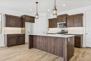 Kitchen featuring backsplash, wood finish floors, an island with sink, and stainless steel appliances