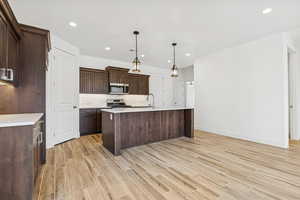 Kitchen featuring dark wood finish cabinets, wood tiled floors, a kitchen island with sink, decorative light fixtures, and stainless steel appliances