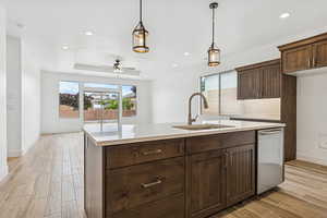 Kitchen with wood finish floors, pendant lighting, a ceiling fan, tasteful backsplash, and stainless steel dishwasher