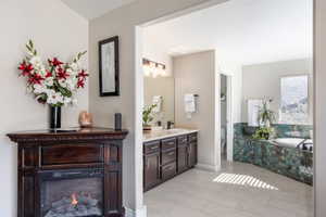 Bathroom featuring a corner electric fireplace, a double vanity with white countertops, and a built-in tub with textured blue-green tile surround