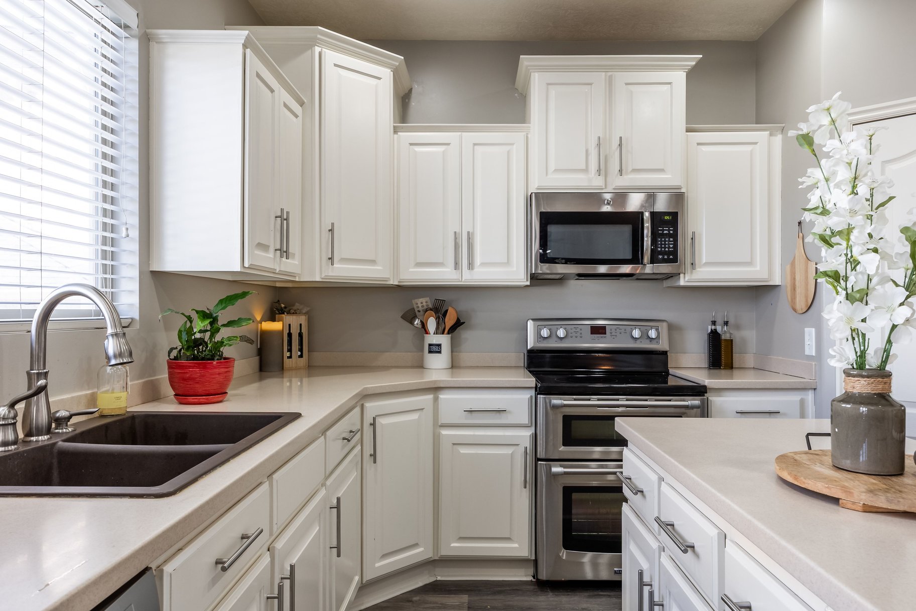 Kitchen featuring white Shaker-style cabinetry, light-toned countertops, a dual-basin sink, stainless steel appliances, and wood-finish flooring