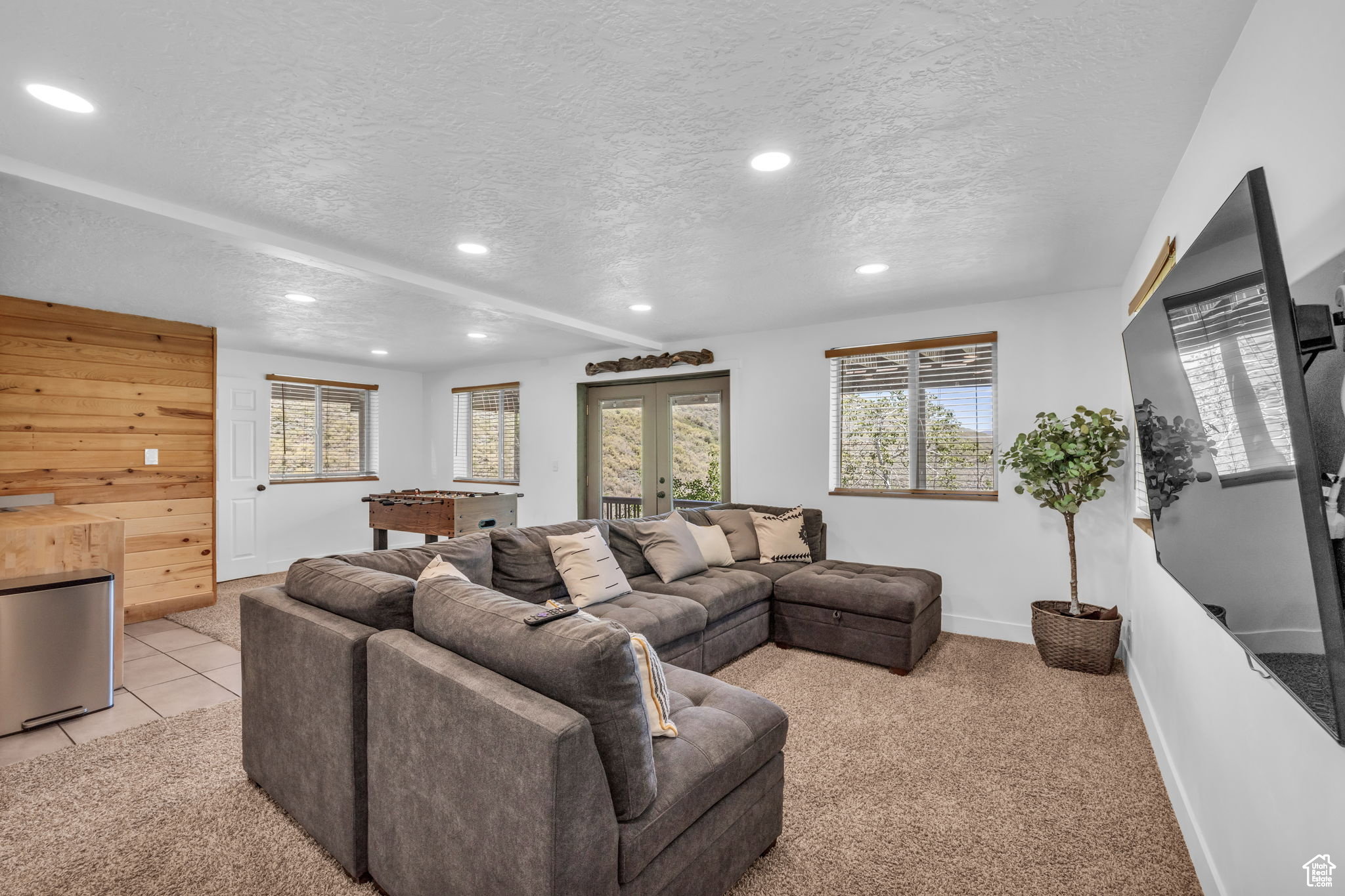 Living room with a textured ceiling, french doors, recessed lighting, light colored carpet, and wood walls