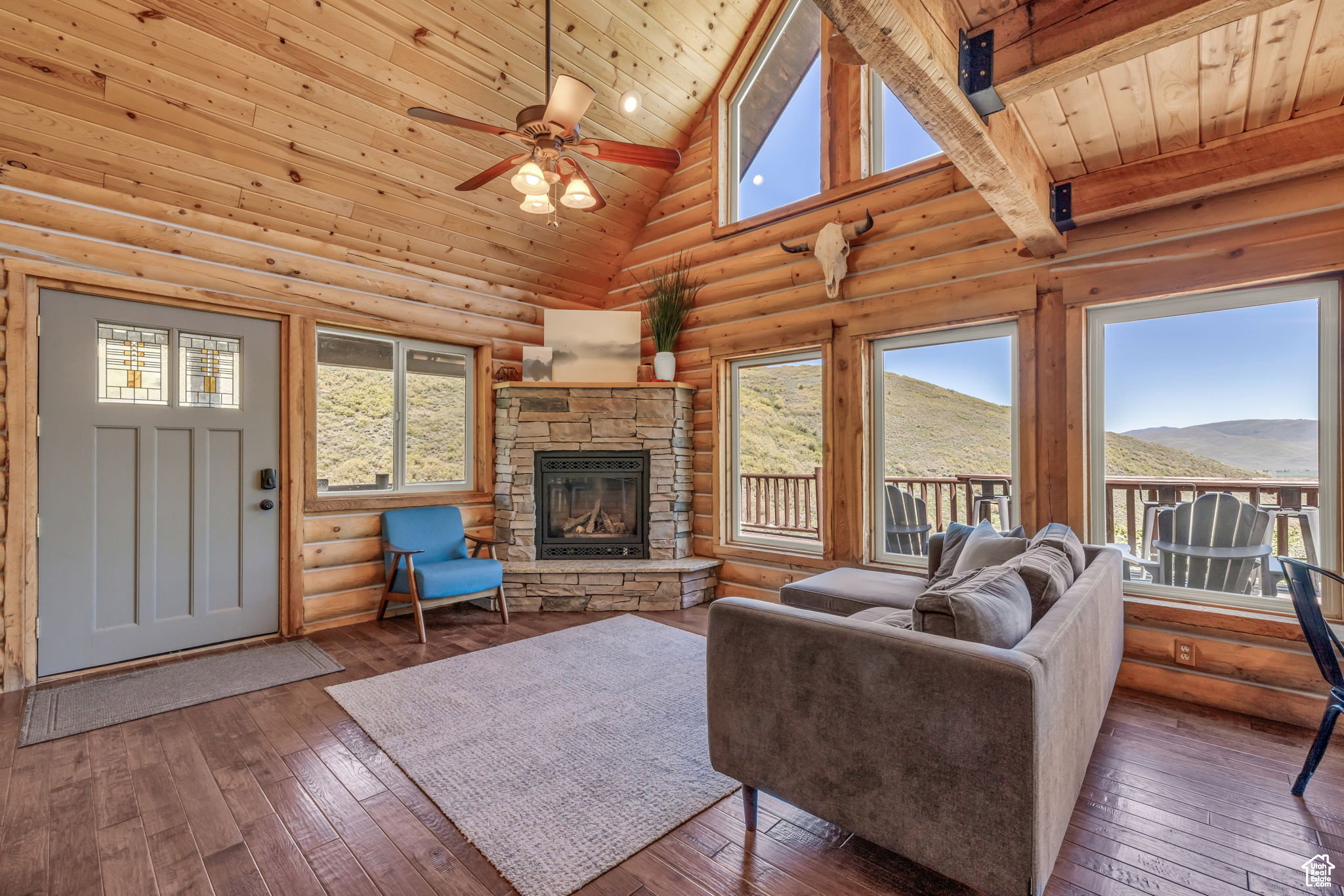 Living room featuring hardwood / wood-style floors, log walls, a fireplace, a ceiling fan, and a vaulted wood ceiling
