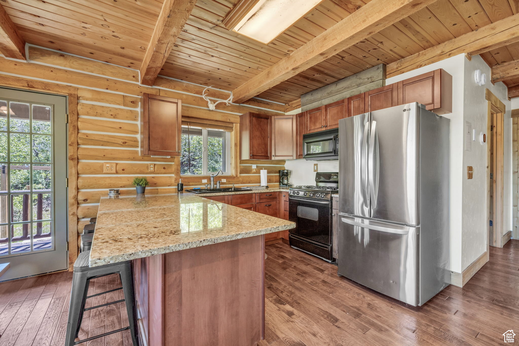 Kitchen with black appliances, light stone counters, a wood ceiling with exposed beams, dark wood-style flooring, and a peninsula