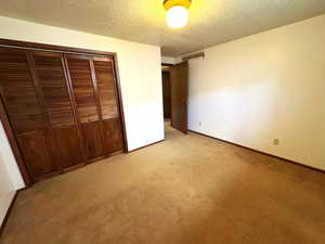 Unfurnished bedroom with a textured ceiling, a closet, and light colored carpet