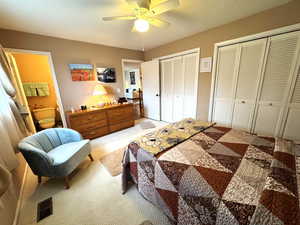 Carpeted bedroom with two closets, ceiling fan, and ensuite bathroom
