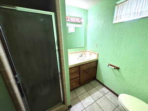 Full bath featuring a textured wall, a stall shower, vanity, light tile patterned flooring, and a textured ceiling