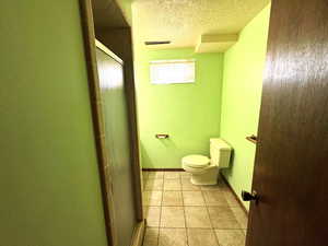 Full bathroom with a textured wall, a textured ceiling, a shower stall, and light tile patterned floors