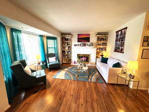 Living area featuring a textured ceiling, dark wood finished floors, a brick fireplace, and built in features