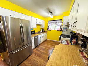Kitchen featuring stainless steel appliances, light countertops, a textured ceiling, dark wood-type flooring, and white cabinetry