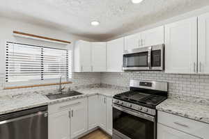 Kitchen featuring stainless steel appliances, light stone counters, white cabinets, light wood-style floors, and recessed lighting