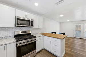 Kitchen featuring a peninsula, stainless steel appliances, white cabinetry, dark wood finished floors, and recessed lighting