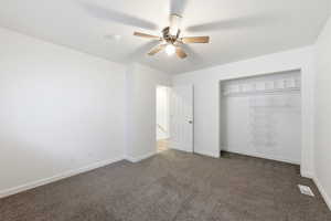 Unfurnished bedroom with dark carpet, a closet, and ceiling fan