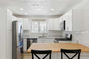 Kitchen with stainless steel appliances, a peninsula, a breakfast bar, white cabinets, and a textured ceiling