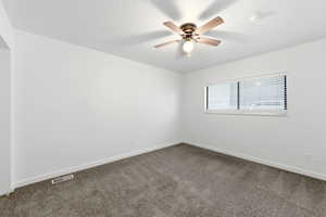 Spare room featuring dark colored carpet and a ceiling fan