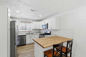 Kitchen featuring a breakfast bar, a peninsula, stainless steel appliances, light wood finished floors, and a textured ceiling