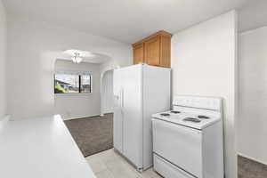 Kitchen featuring white appliances, light colored carpet, arched walkways, light countertops, and wood finish cabinets