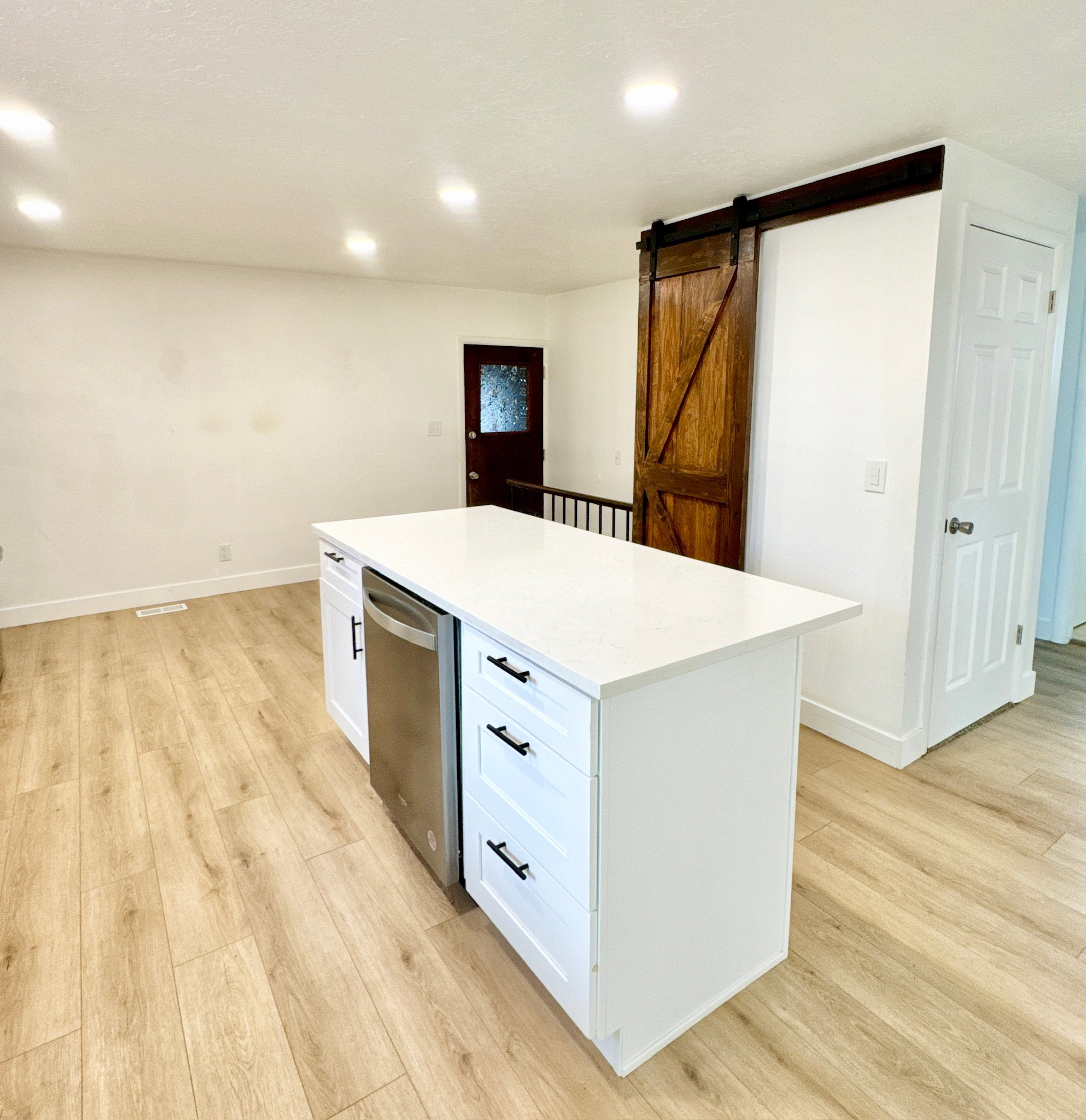 Kitchen featuring a barn door, a kitchen island, light wood-type flooring, stainless steel dishwasher, and recessed lighting