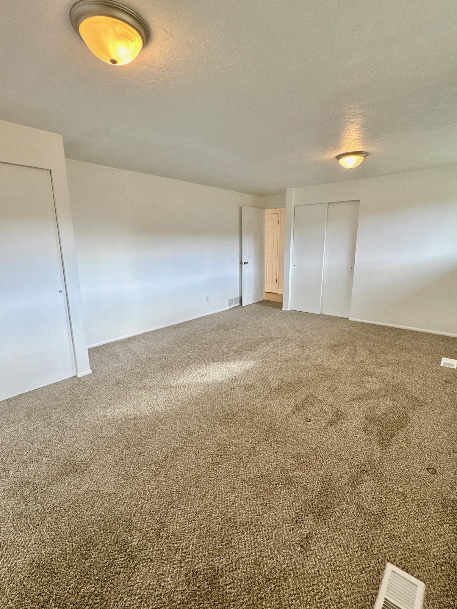 Unfurnished bedroom with a textured ceiling, carpet floors, and two closets