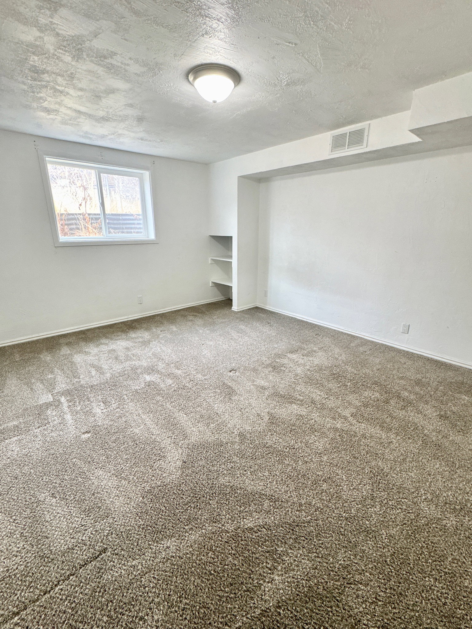 Carpeted empty room with a textured ceiling and baseboards
