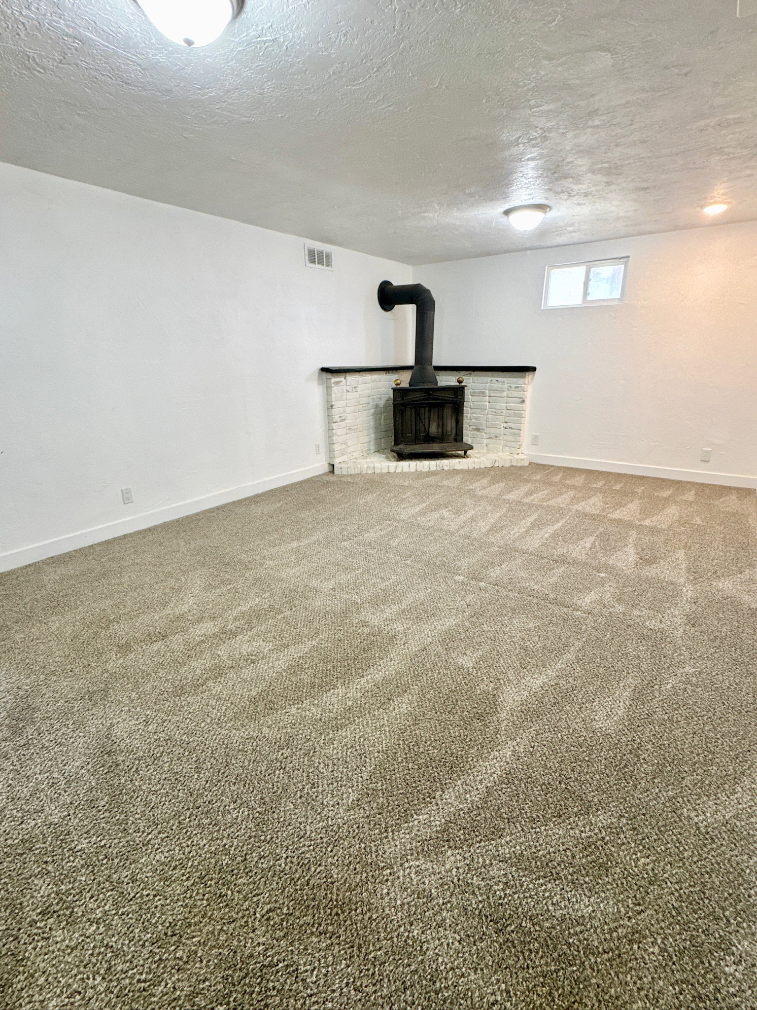 Below grade area featuring a textured ceiling, carpet, and a wood stove