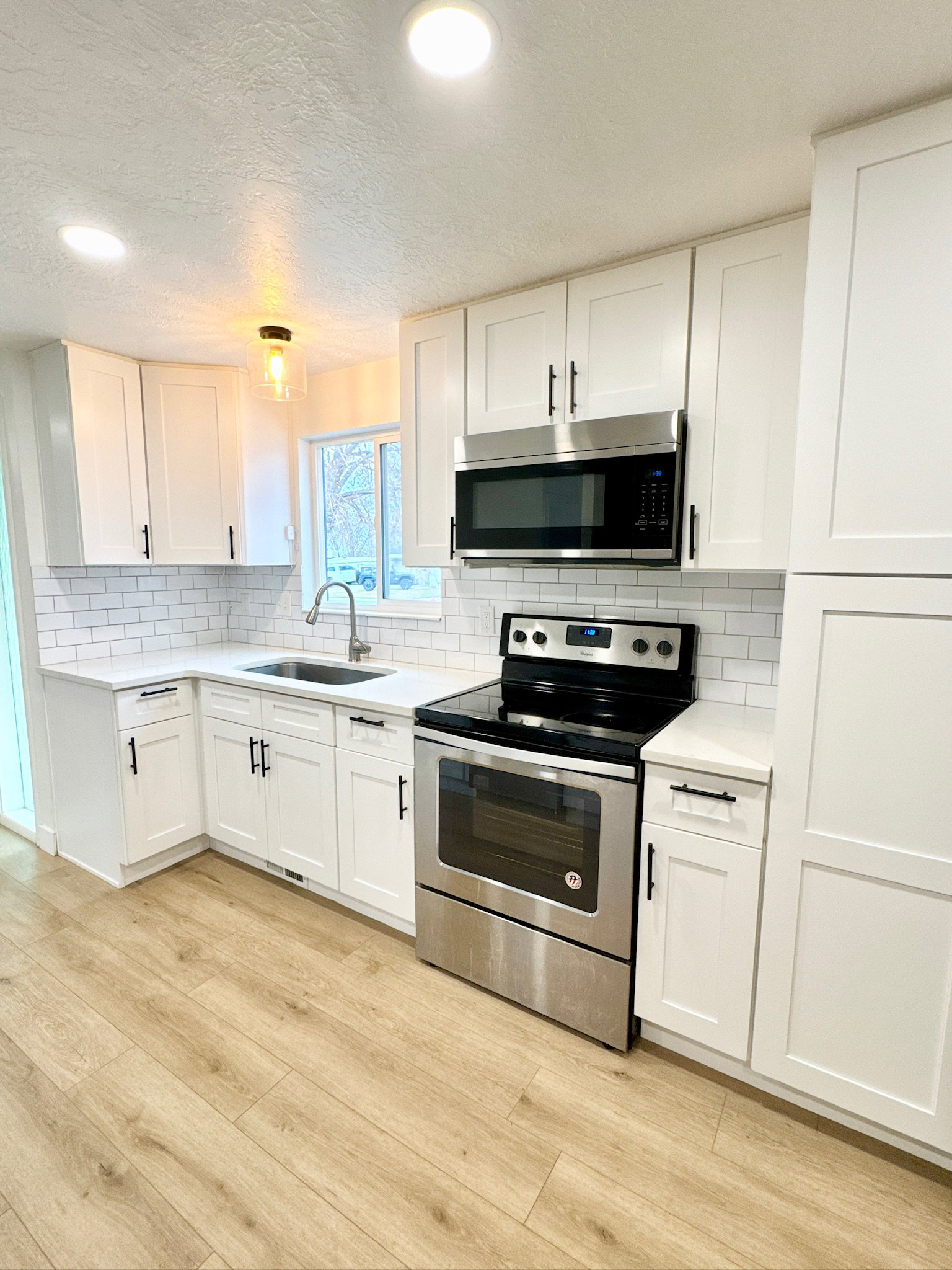 Kitchen with stainless steel appliances, white cabinets, light wood-style floors, tasteful backsplash, and a textured ceiling