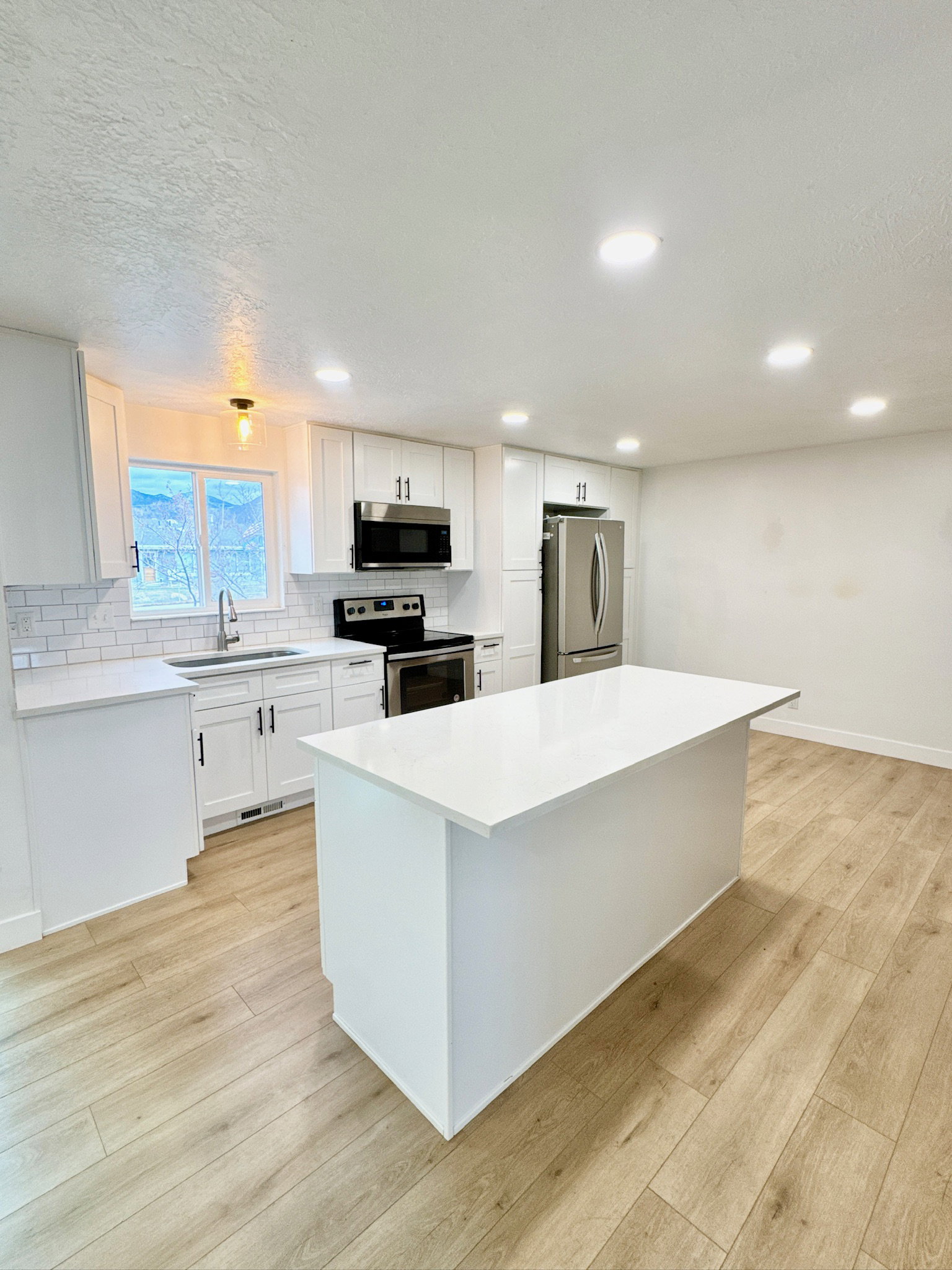 Kitchen featuring stainless steel appliances, light wood-type flooring, a kitchen island, white cabinetry, and a textured ceiling