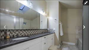 Full bathroom with double vanity, a baseboard radiator, decorative backsplash, and a bath
