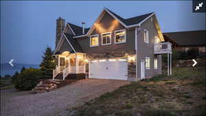 View of front of house featuring gravel driveway, an attached garage, a chimney, and stone siding