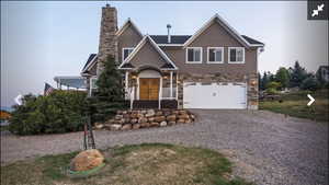 View of front of house with gravel driveway, a garage, stone siding, and a chimney