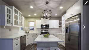 Kitchen with stainless steel appliances, open shelves, white cabinets, glass insert cabinets, and light stone counters