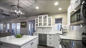 Kitchen with stainless steel appliances, light stone counters, a kitchen island, white cabinets, and glass insert cabinets