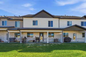 Back of house with board and batten siding, stone siding, a yard, and a shingled roof