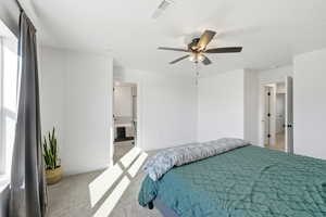 Bedroom featuring a ceiling fan, ensuite bath, and light carpet