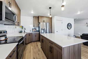 Kitchen featuring stainless steel appliances, light wood-type flooring, a kitchen island, backsplash, and pendant lighting